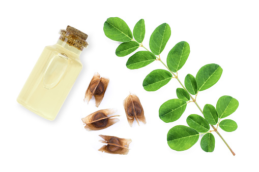 Moringa oil, moringa seeds and moringa leaves with a white background.